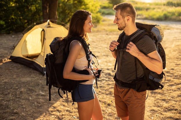 a man and a woman in a hiking trip with backpacks near a tent at sunset. honeymoon in nature