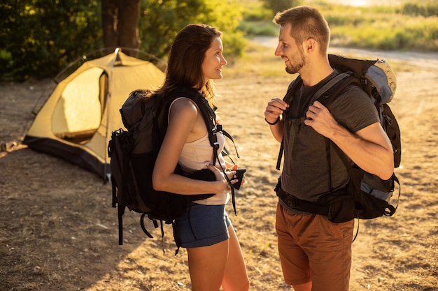 Un uomo e una donna in un'escursione con zaini vicino a una tenda al tramonto. luna di miele in natura