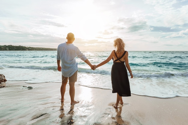 Man and a woman hold hands and watch the sunset on the beach