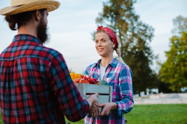 A man and a woman holding a box with a crop of farm vegetables  of the garden.