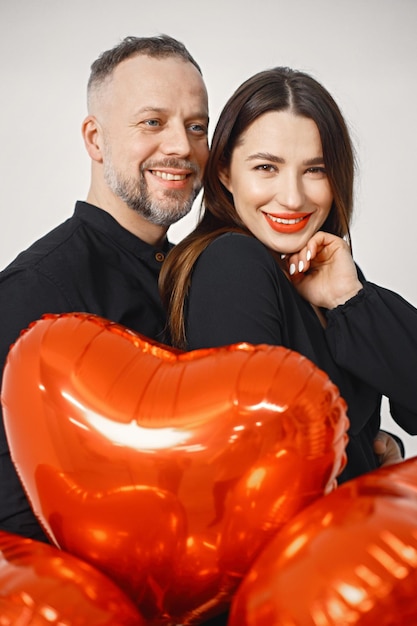 Man and woman holding bunch of heartshaped red ballons and posing in studio