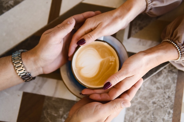 Uomo e donna che tengono le mani su una tazza di caffè