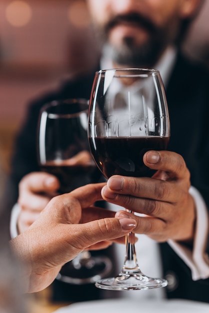 Uomo e una donna che tiene insieme un bicchiere di vino rosso in primo piano.