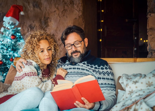 Man and woman at home enjoying holiday season and christmas time having relax leisure indoor activity together People in relationship Mature male reading a book Female hugging husband and smile