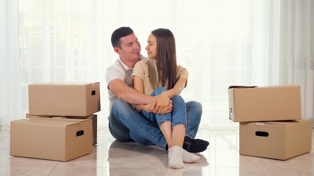 Man woman in jeans sit on light floor in new house hugging