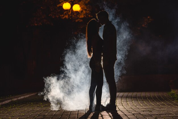 男と女は煙の背景で路上でキスします。夜の時間
