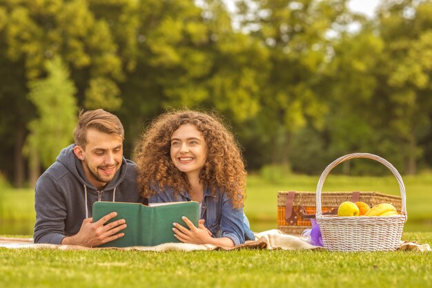 Мужчина и женщина лежали на траве и читали книгу в парке