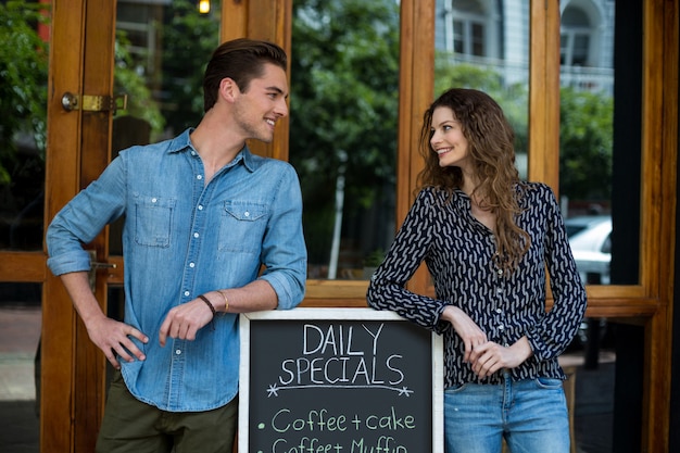 Man and woman leaning on menu board outside the coffee