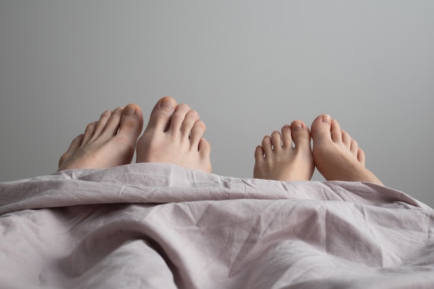 ベッドの上の男性と女性の足。ベッドでカップルの足、クローズアップ。おはようございます。