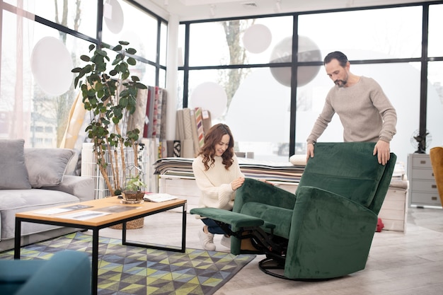 Man and woman in light sweaters examining a big green armchair