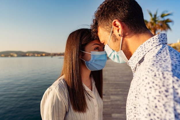 Man and woman look into each other's eyes by leaning foreheads against each other wearing protective mask due to Coronavirus.