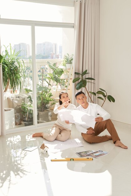 Photo man and woman looking at their house plans sitting in their new house