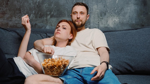 A man and a woman in love are lying on the couch and watching their favourite show on TV