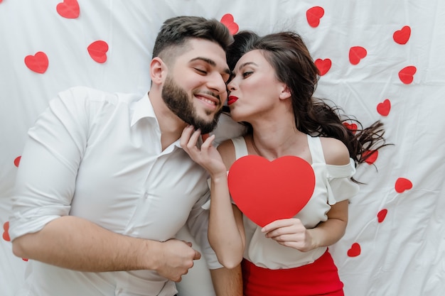 Man and woman in love on bed with red heart shaped valentine card at home