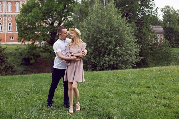 Man and a woman in love in a dress and hat are stand on a green field under a tree in summer