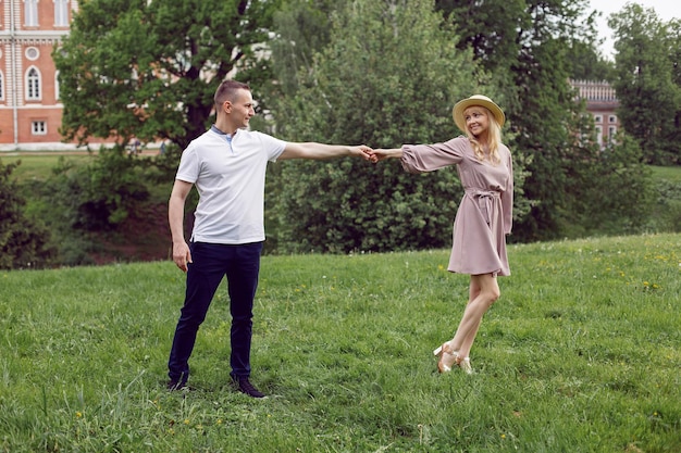 Man and a woman in love in a dress and hat are walk on a green field under a tree in summer