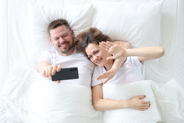 ベッドに横になって自分撮りの上面図を撮る男と女