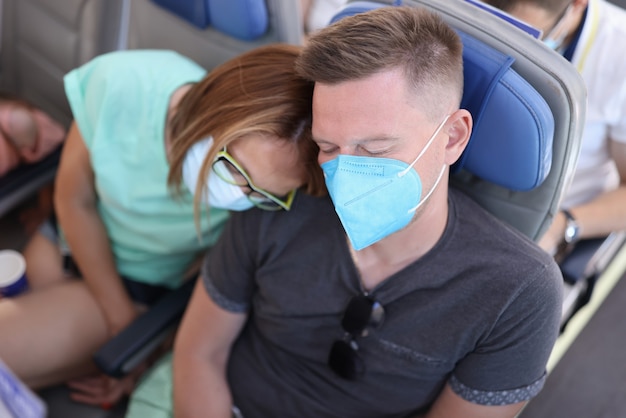 Man and woman in medical protective masks are sleeping in aircraft cabin