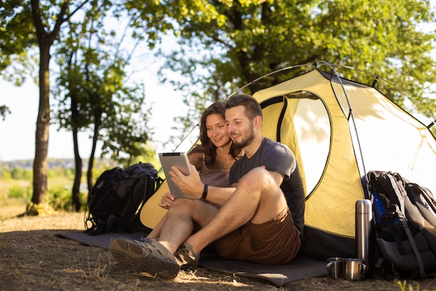 A man and a woman near the tent with a tablet. They talk on video communication with friends