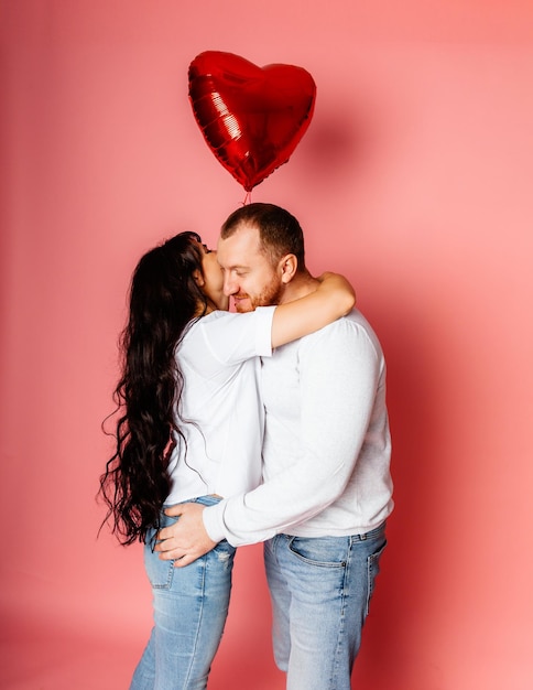 A man and a woman on a pink background hold a large inflatable red heart-shaped balloon in their hands. holiday concept - valentine's day