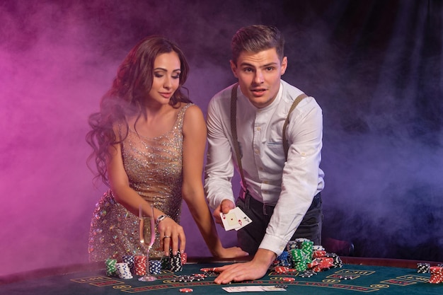 Uomo e donna che giocano a poker al casinò celebrando la vittoria al tavolo con pile di carte chip champagne