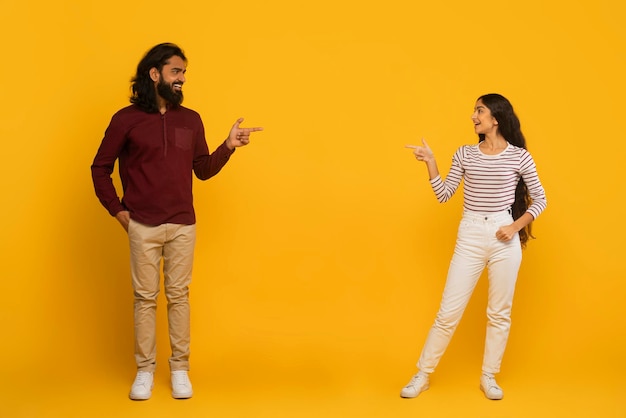 Man and woman pointing each other on yellow background