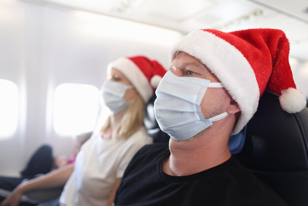 Man and woman in protective masks and santa hats flying in airplane