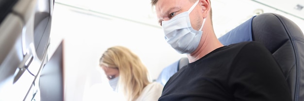 Man and woman in protective masks working on laptops in aircraft cabin