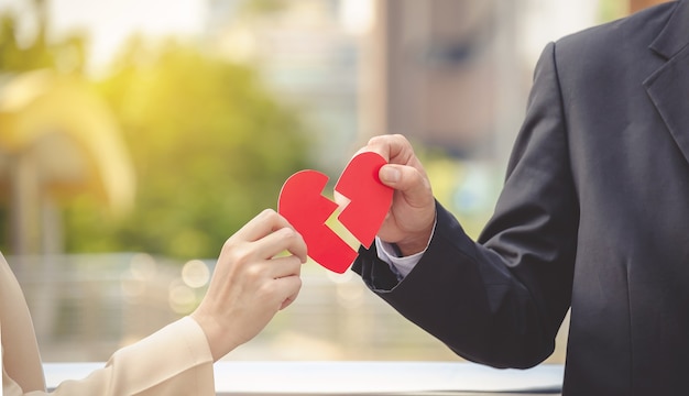 Man and woman pulling a red paper heart apart. The concept of unrequited love. Broken hear