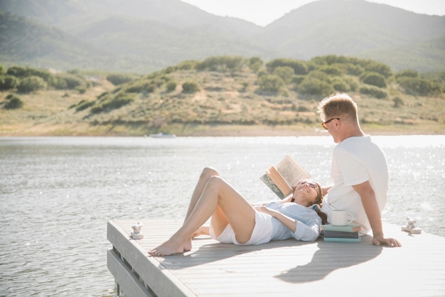 Man and woman reclining on a jetty reading a book