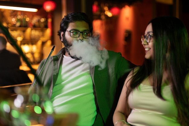 Photo man and woman relaxing by vaping from a hookah in a bar