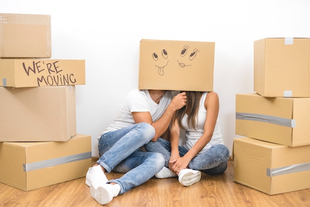 The man and woman sit on the floor with a carton box on the heads