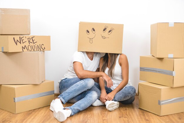 The man and woman sit on the floor with a carton box on the heads