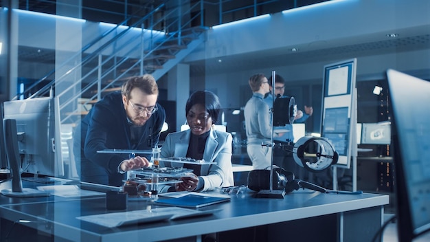 A man and woman sit at a table in a lab with a model of a drone.