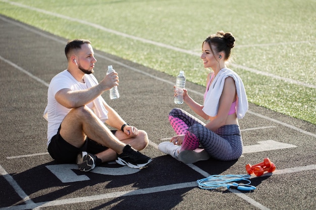 Man and a woman sit on the treadmills after a run at the stadium in the summer they listen to music