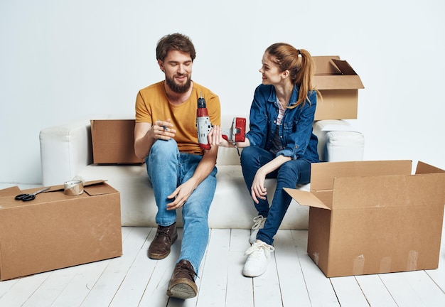 Man and woman sit on white couch boxes with moving lifestyle things