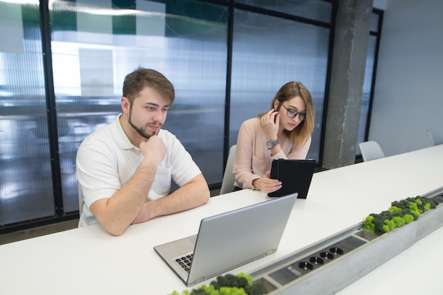 Man and woman sit with gadgets at work.