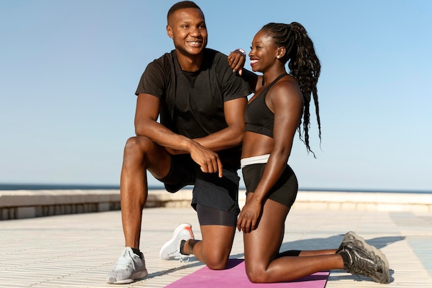 Man and woman sitting near the water and embracing with each other after morning trainings