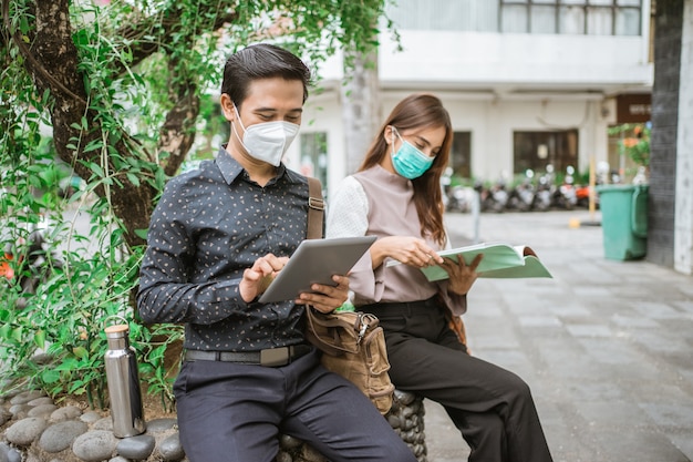 Man and woman sitting on the park bench with tablet