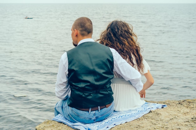 man and woman sitting on a stone and looking at the sea