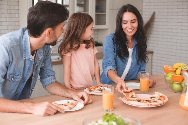 男と女と小さな女の子が一緒に自宅のキッチンで夕食にピザを食べる