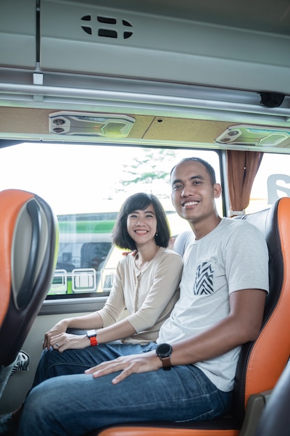 A man and a woman smile while sitting together in a bus seat while traveling