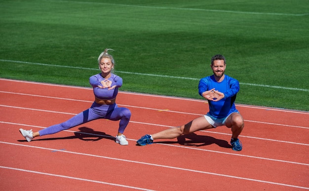 男性と女性のスポーツトレーナー。屋外でトレーニングするフィットネスカップル。ストレッチ運動とウォーミングアップ。両方のトレーニングチャレンジ。スタジアムの深いスクワット。チームワーク。スポーティーな人にフィットします。