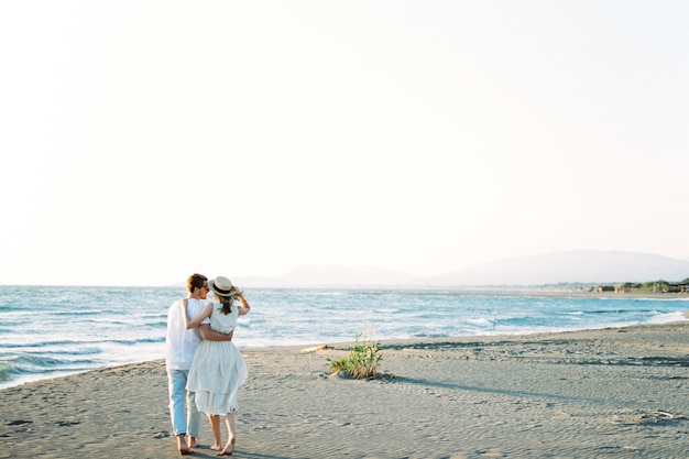 Man and woman stand embracing on the beach by the sea Back view