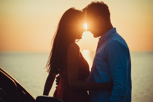 The man and woman standing near the car on the sea shore