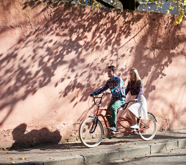 man and woman on tandem bicycle on red wall