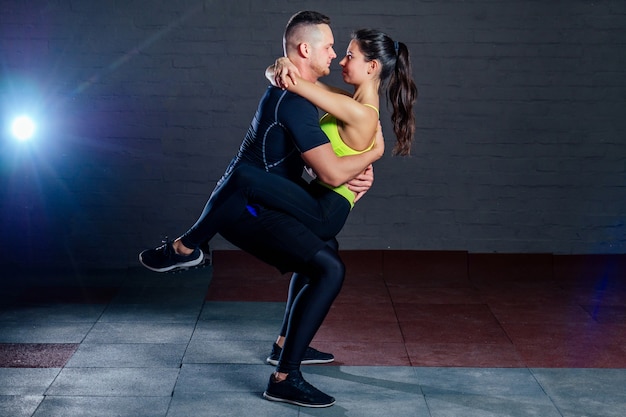 Foto uomo e donna si allenano insieme in palestra su uno sfondo di mattoni neri. sit-up cooperativi