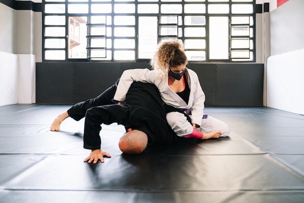 Man and woman training martial arts and judo with kimonos on the gym floor mat with a face mask because of the covid 19