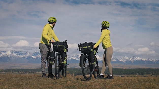 男と女はバイクパッキングで混合地形サイクルを旅します自転車バッグを持った自然の中でテントを持った愛のカップルの旅グリーンブラックカラーのスタイリッシュなバイクパッキングバイクスポーツウェア