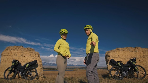 The man and woman travel on mixed terrain cycle touring with bikepacking The two people journey with bicycle bags Mountain snow capped stone arch